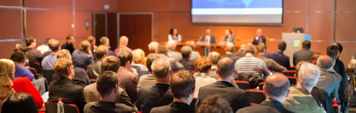 a crowd sat in a conference hall listening to speakers on stage