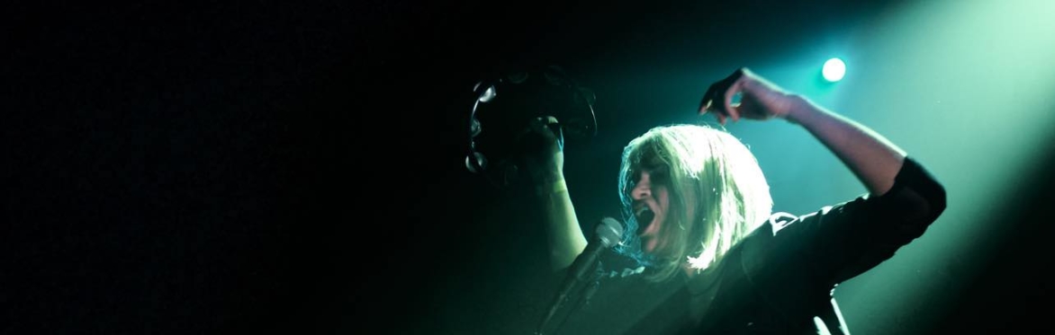VICE VERA with arms raised, holding a tambourine, singing into a mic
