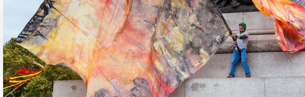 Person holding large abstract banner showing flame and burning colours, on stone steps