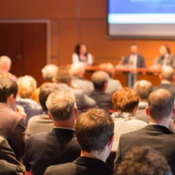 a crowd sat in a conference hall listening to speakers on stage