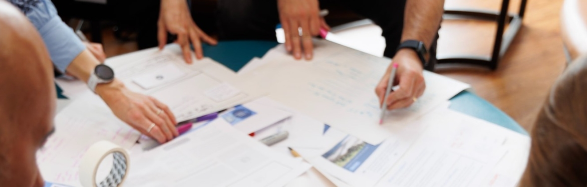 Photo focussing on arms and hands of a group of people working with paper, scissors and graphics.