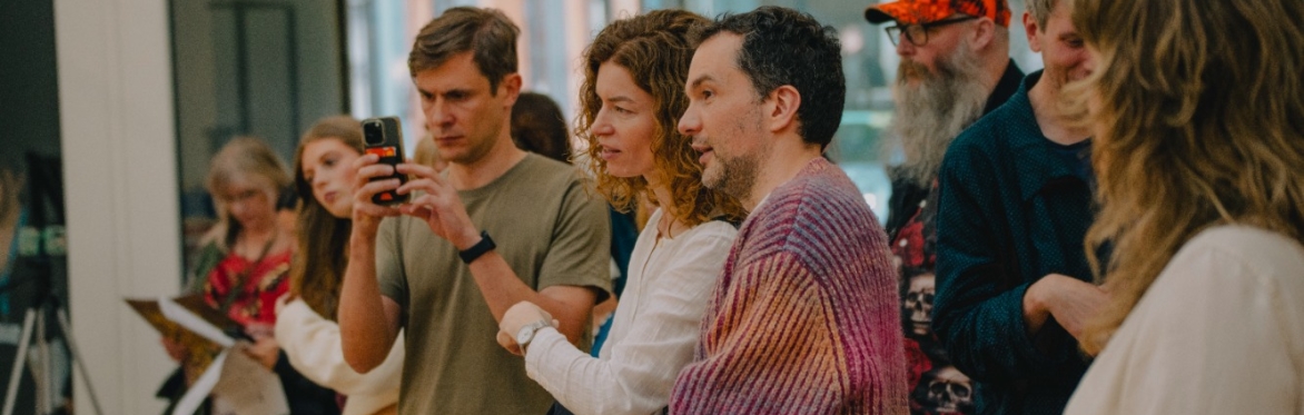 A group of people chatting and looking onto an exhibition that is not visible in the image. Someone is taking a photo on the their phone.