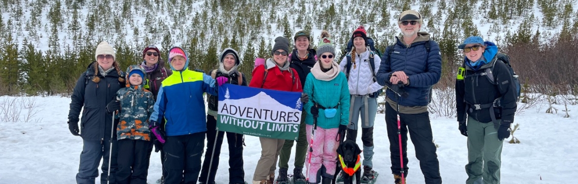 A large group of participants, staff, and volunteers pose together in front of snowy Mt Hood on an inclusive and adaptive snowshoe trip