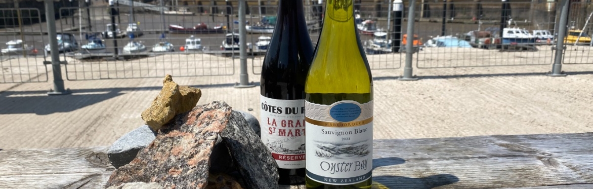 A bottle of red and white wine displayed next to rocks.