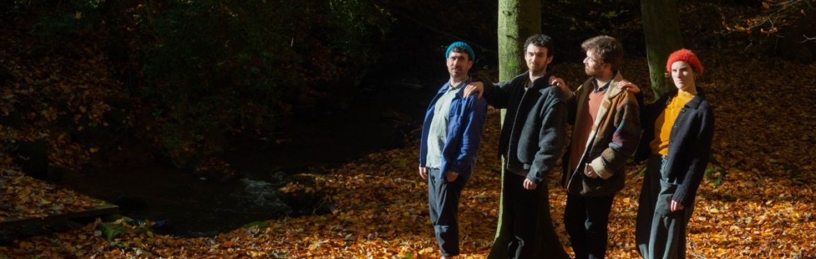 A group of four bandmates stand together in an autumnal forest.