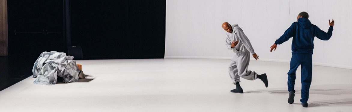 Two men dance on a stage, to their left is a ball of fabric