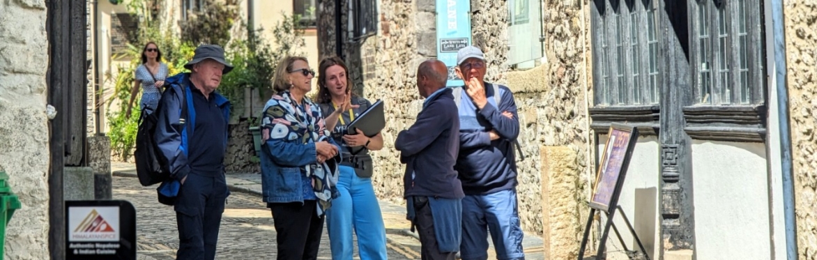 A woman talks to a group of four people on a narrow Elizabethan street.