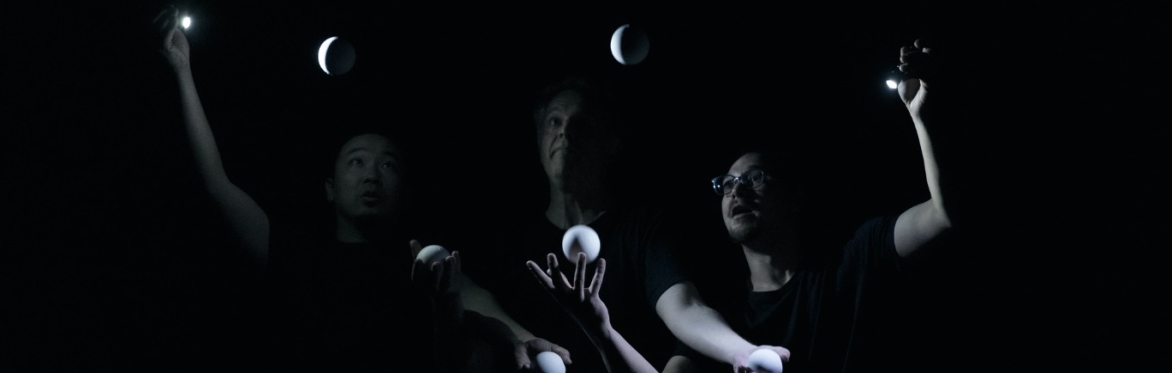 three ball jugglers in a hauntingly beautiful ensemble. they all stare intently at the balls in the air while their hands are engrossed in a flurry of activity.