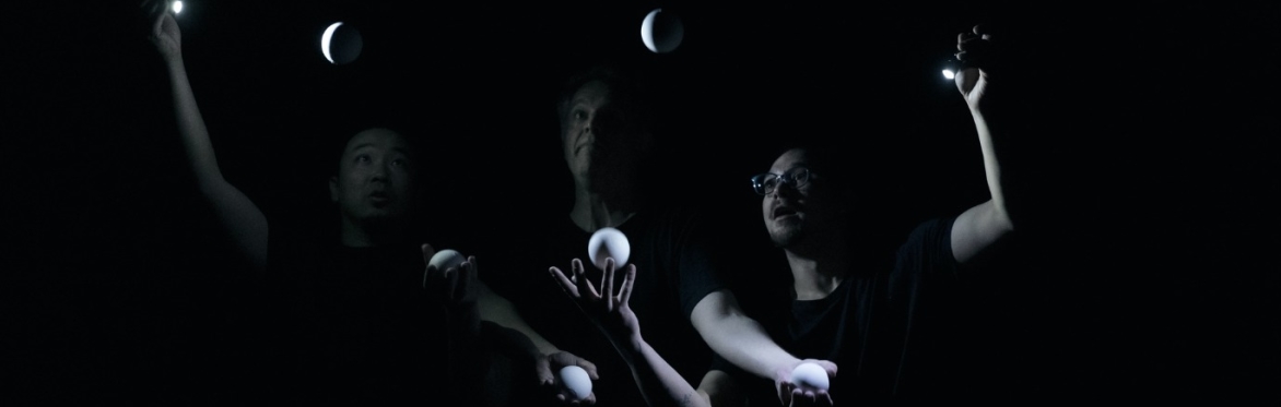 three ball jugglers in a hauntingly beautiful ensemble. they all stare intently at the balls in the air while their hands are engrossed in a flurry of activity.