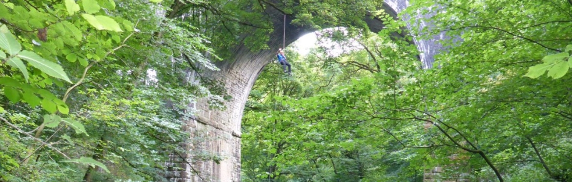Image of a person dangling on a rope as they abseil below a viaduct.