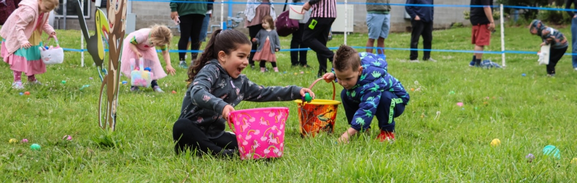 Multiple kids search for colorful eggs in a grassy field.
