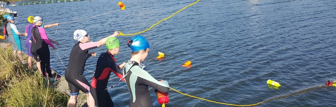 Young lifesavers wearing wetsuits use throw bags next to the river