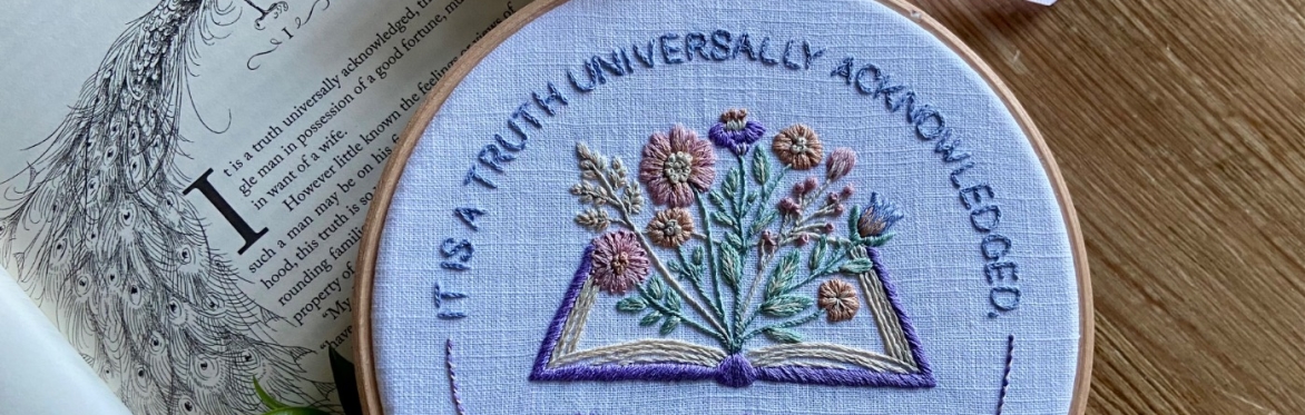 Embroidery hoop with a pastel open book and flowers design, featuring a Pride and Prejudice quote, finished with lilac ribbon on an illustrated page.