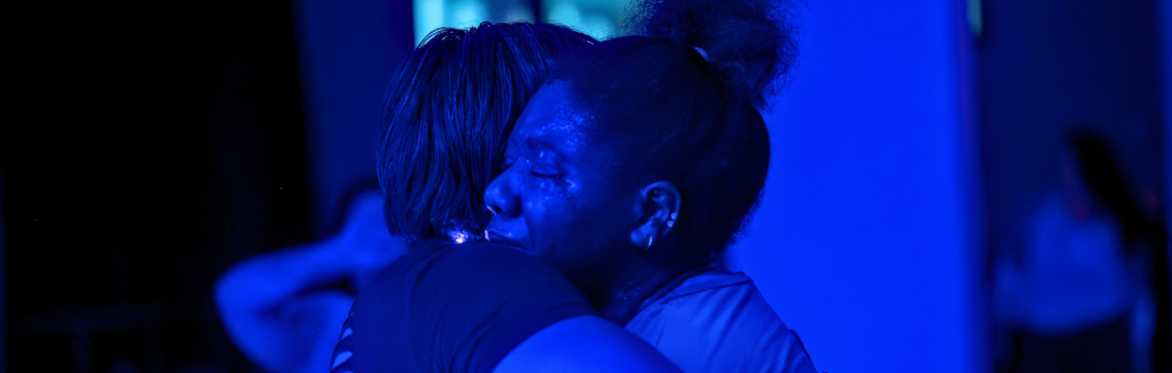 Black woman with eyes closed and tears being held by another woman.