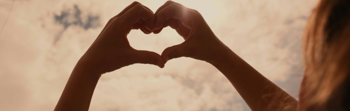 Hands in the shape of a heart against a light-filled sky
