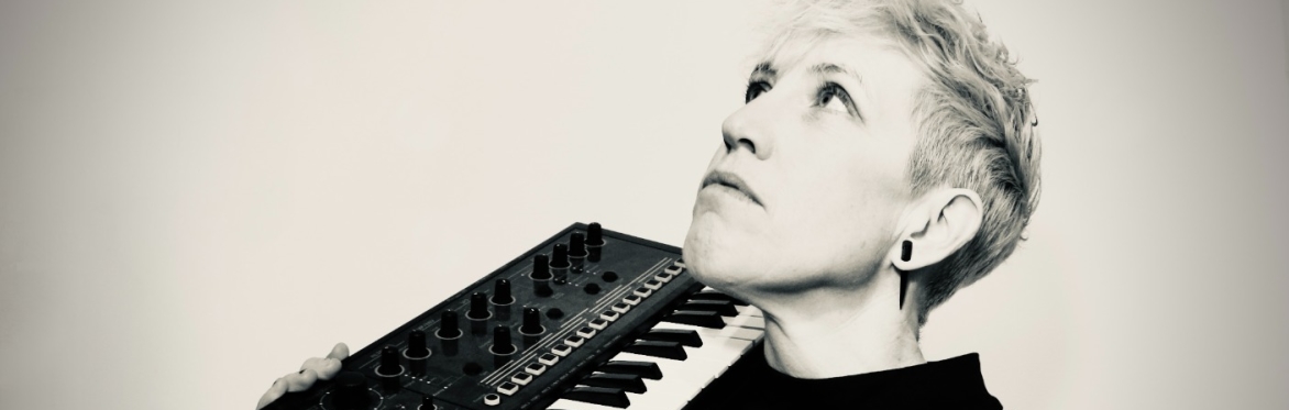 Person holding a small keyboard synthesizer on their shoulder, looking upward.