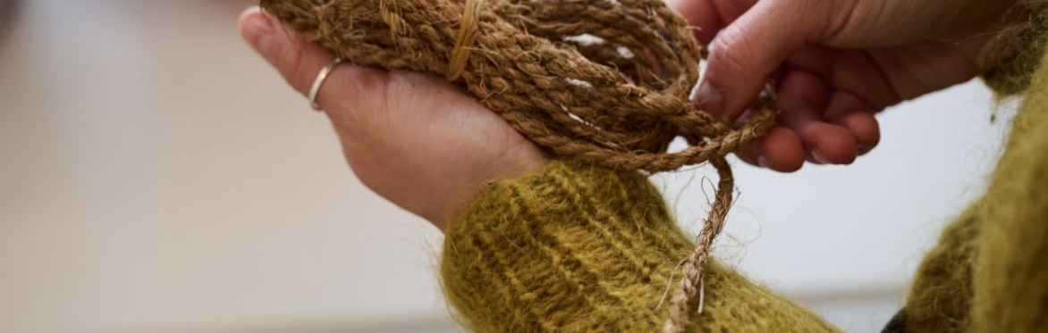 Close up photograph of hands delicately holding a ball of hop yarn. Person is wearing a mustard coloured mohair jumper.