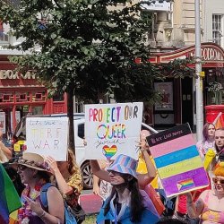 Bristol Pride Parade 2022: a group of people hold rainbow flags and signs as they march past the Bristol Hippodrome