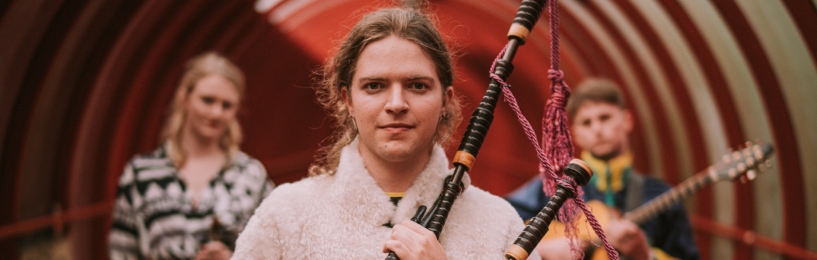 Malin Lewis in a tunnel holding a set of Highland bagpipes with Sally Simpson and Lucy McNally blurred behind him