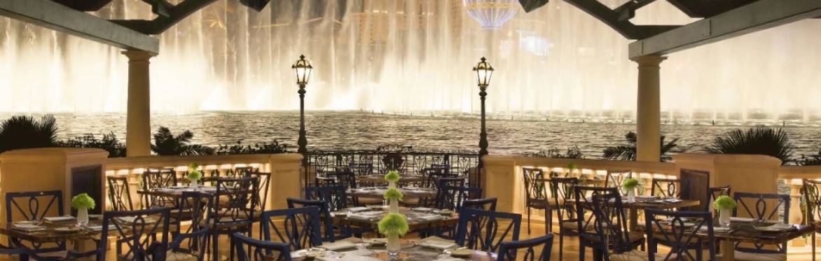 Elegant dining terrace with views of the Fountains of Bellagio and the Las Vegas Strip at night.