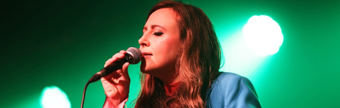 Siobhan singing into microphone onstage with a green background
