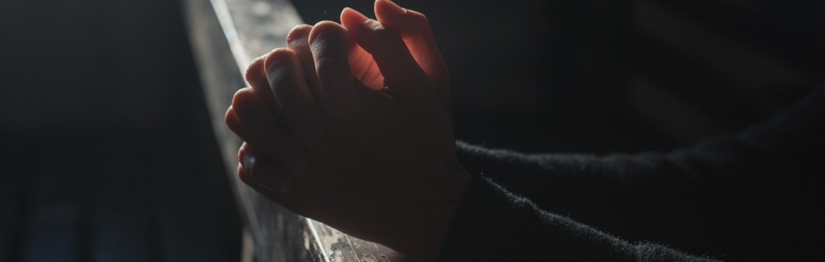 Hands held in a classic prayer pose, resting on what looks like a church pew