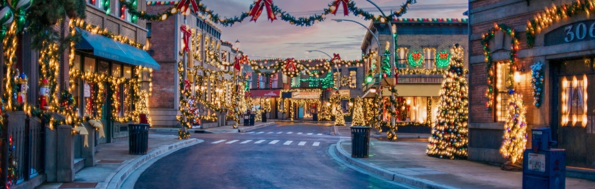 Festive New York-style street at Merry & Bright in Martini Town, decorated with Christmas lights, garlands, bows, and glowing holiday trees at dusk.
