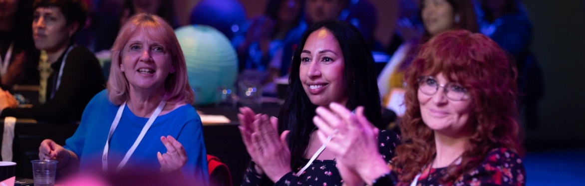 A group of people smiling and clapping. Sat down at an Awards event.