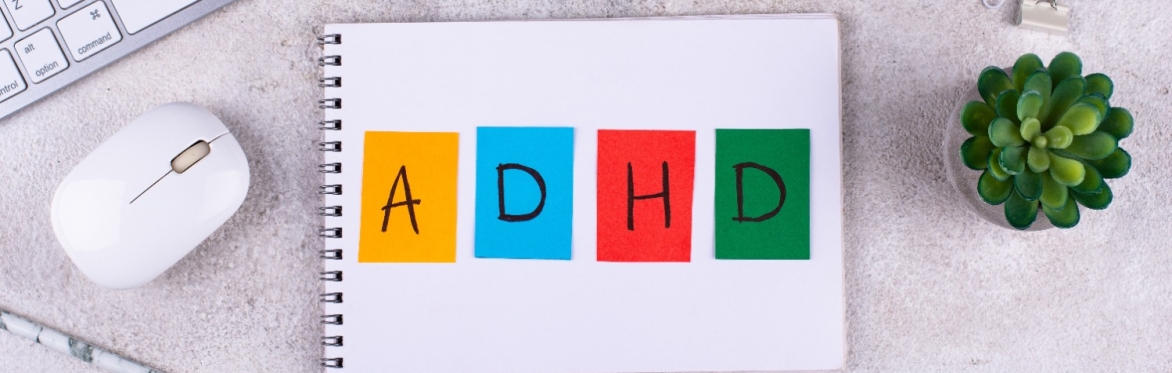 Notepad with ADHD written on it, next to laptop and plant on desk