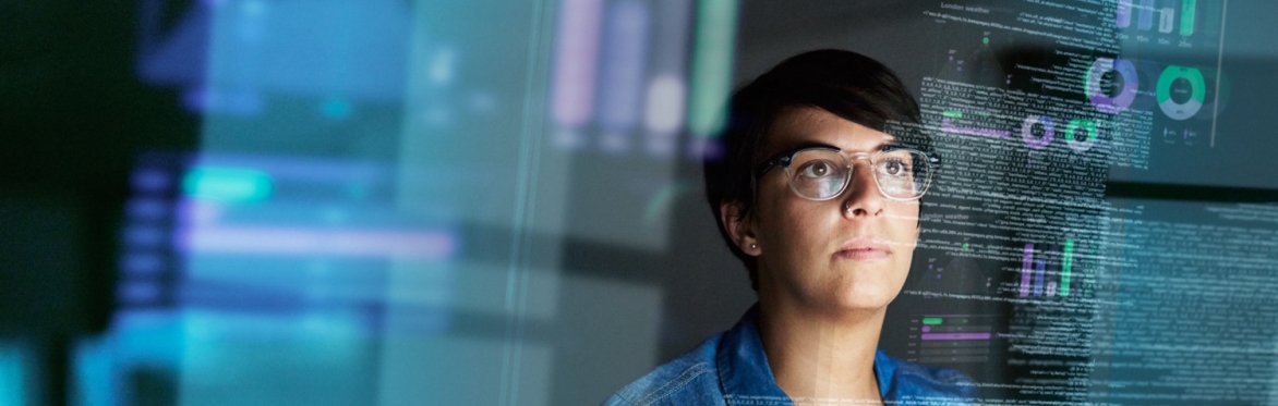 Woman with short brown hair and clear framed glasses sitting behind a clear glass that shows data and graphs.