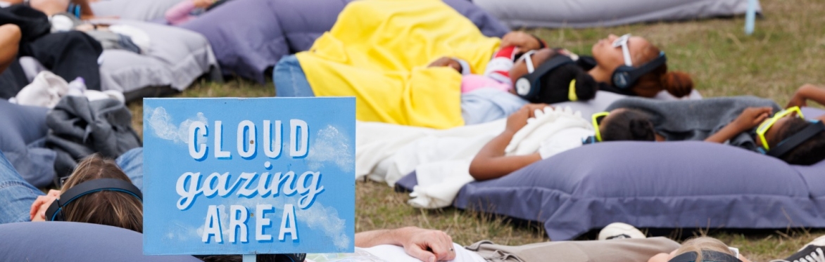People of all ages and backgrounds lying on beanbags looking at the sky. Sign saying Cloud Gazing Area