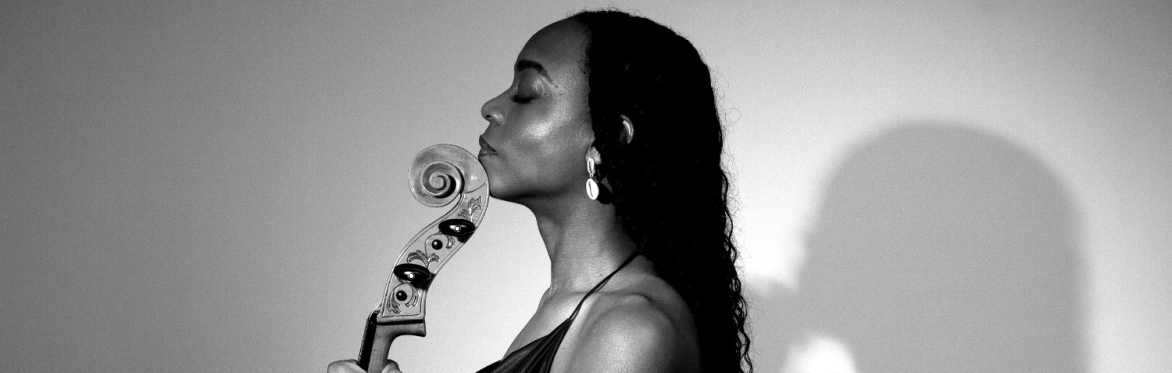 A side profile, black and white photo of Ayanna Witter-Johnson, holding her Cello against a plain backdrop