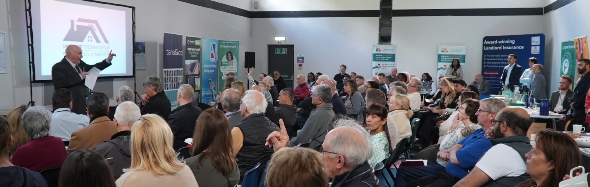 Attendees at the landlord forum sat in rows, watching a presentation from one of the speakers who is stood at the front, holding a microphone