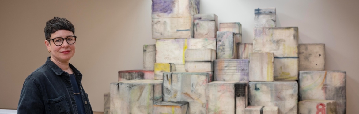 The artist Eva Rothschild stands beside her work Amphi that are colourful large blocks piles high by the back wall.