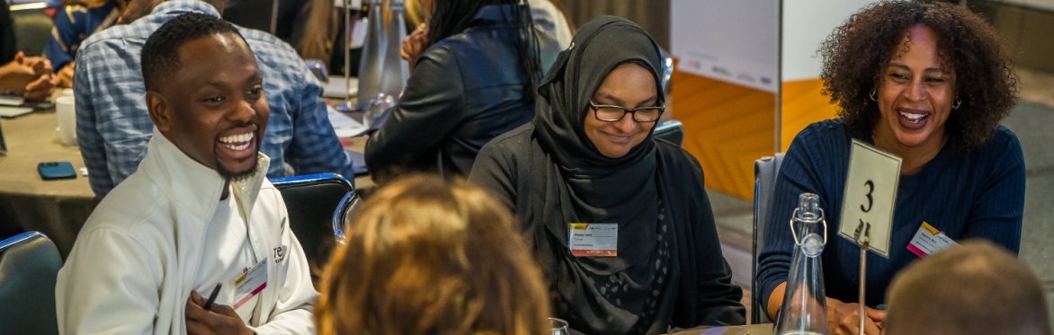A group of people seated around tables at a business networking event, engaged in conversation over breakfast.