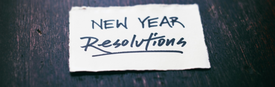 A white card with "New Year Resolutions" written on it, on a dark wood table.