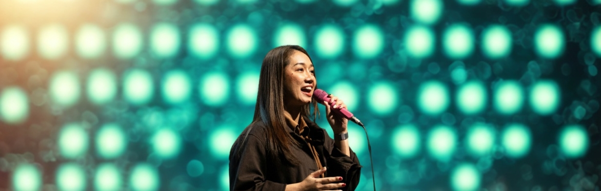A smiling woman is singing into a microphone and gesturing