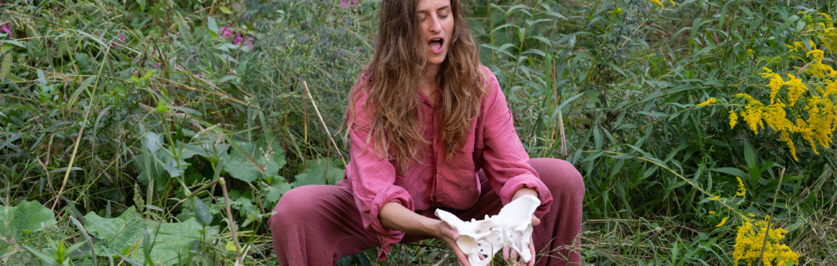 A woman in squat, holding pelvic bones in front of her and sounding with eyes closed.