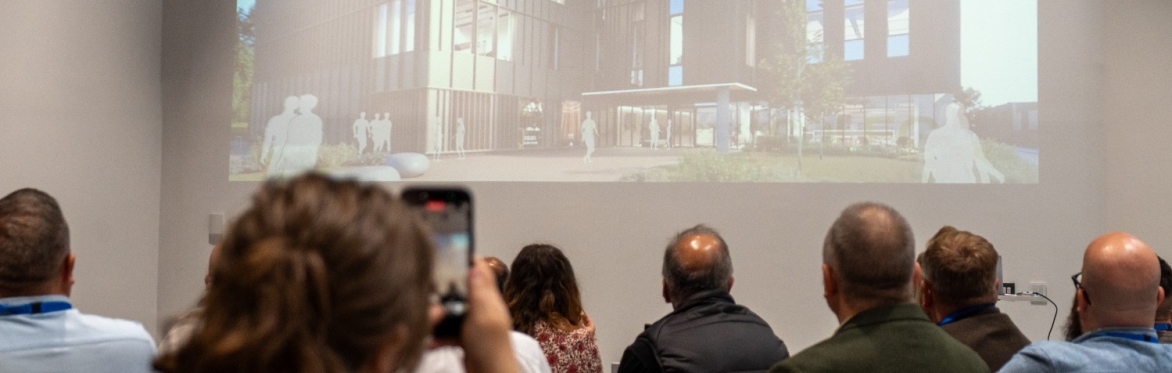 Audience watching a projection of a modern building design on a screen during a presentation.