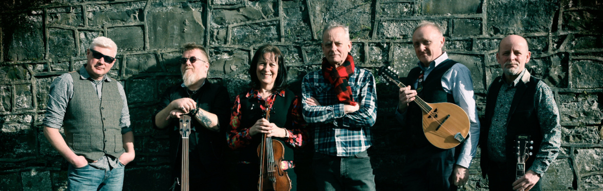 Six attractive bluegrass band members posing deliciously beside a  wall