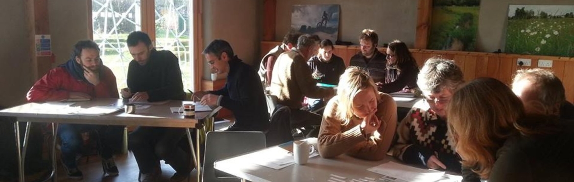 A group of people, working in groups, sitting at tables in a naturally built space