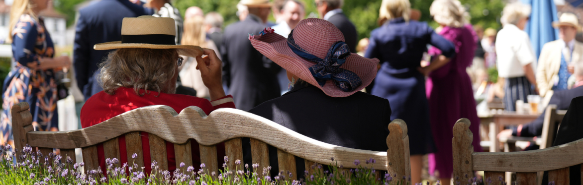 Regatta visitors sitting on a sunny bench in straw hats