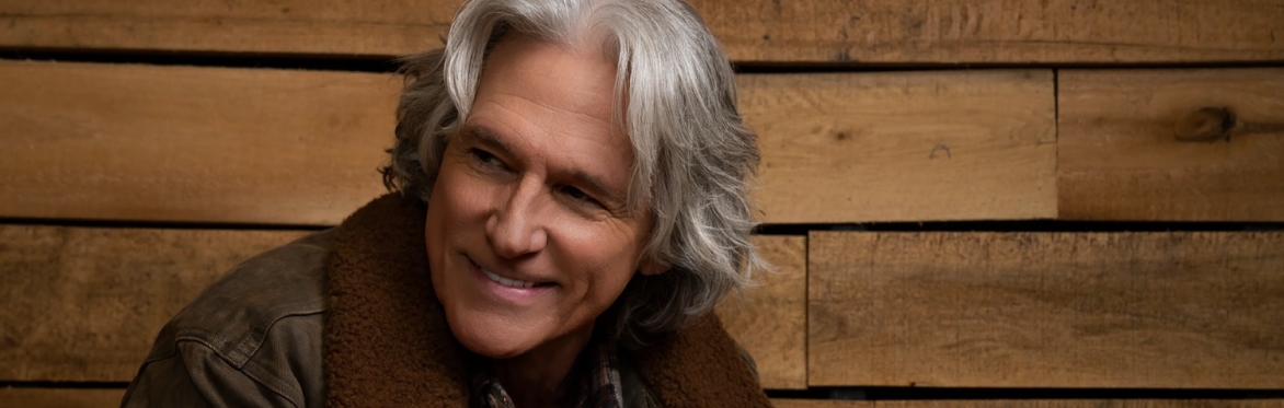 Billy Dean smiling in front of a wood panel background
