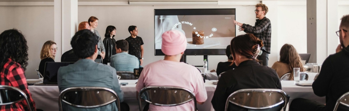 3 people sat on chairs looking at a man presenting.