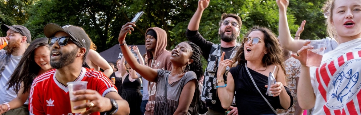 A group of men and women enjoying an outdoor music event in a park.