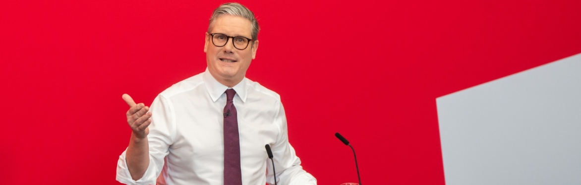 A man (Keir Starmer, British Prime Minister) stands at a lectern in a suit with a red background