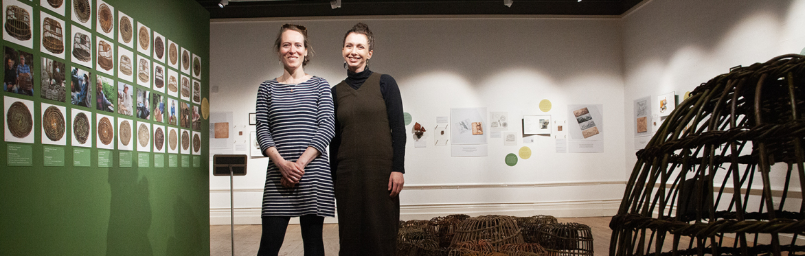 Two people stood in an exhibition of withy pots
