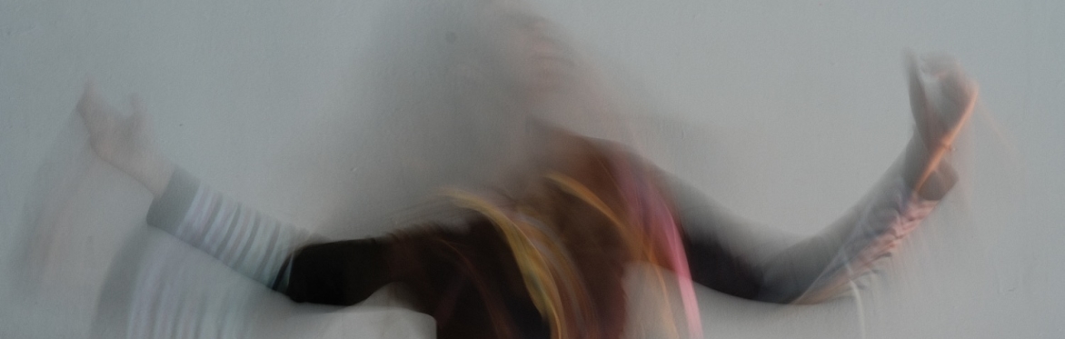 Abstract blurred figure in motion, with extended arms suggesting fluid movement and expressive physicality.