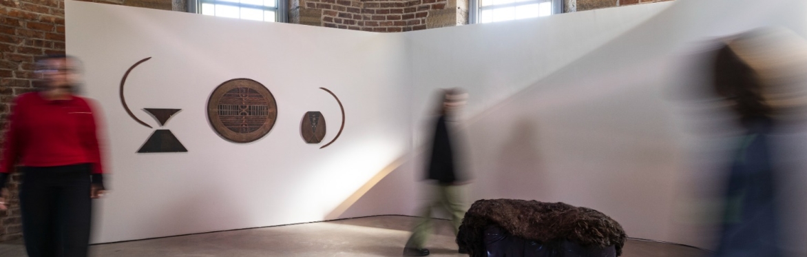 A blur of people move past a pink and black piece of art hung on a red brick wall