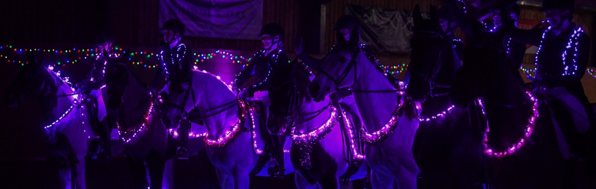 Riders on horses decorated with Christmas lights performing together in an indoor arena